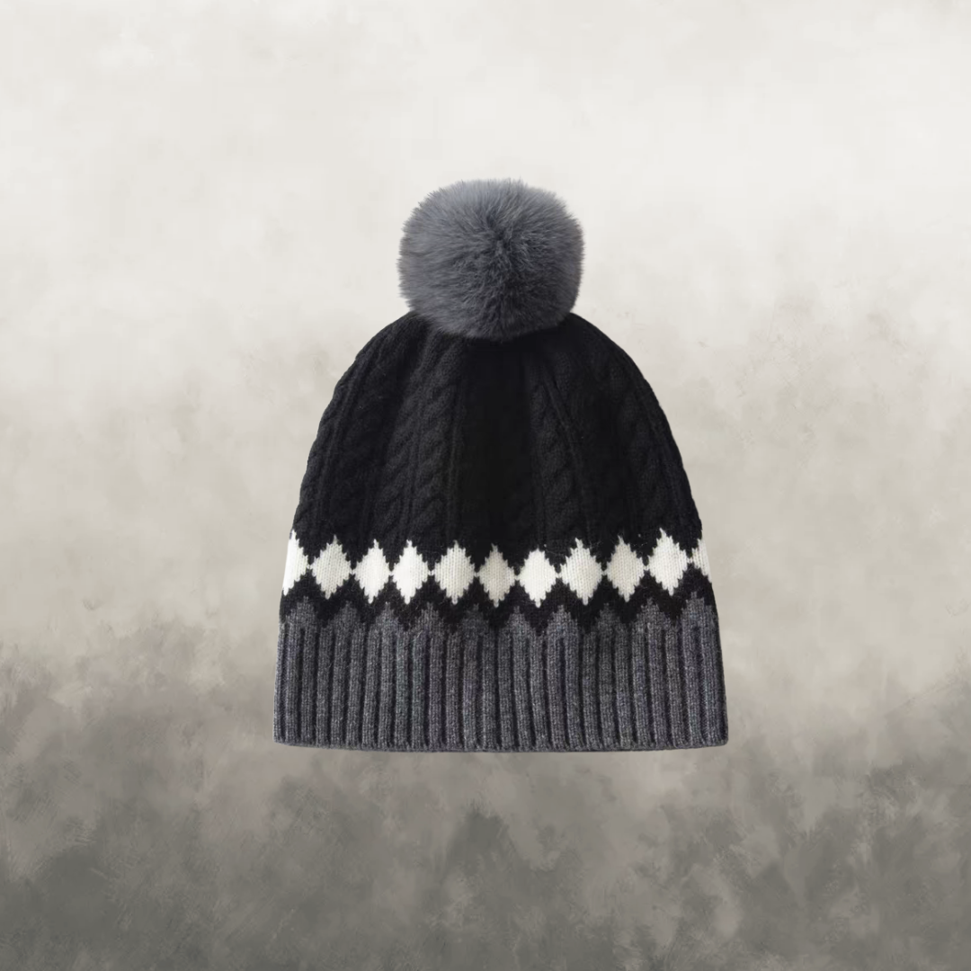 Black knit beanie with gray pom-pom on a textured gray background