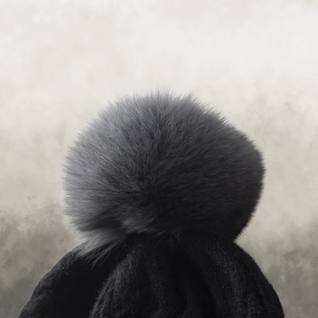 Black beanie with a large gray fur pom-pom on a neutral background
