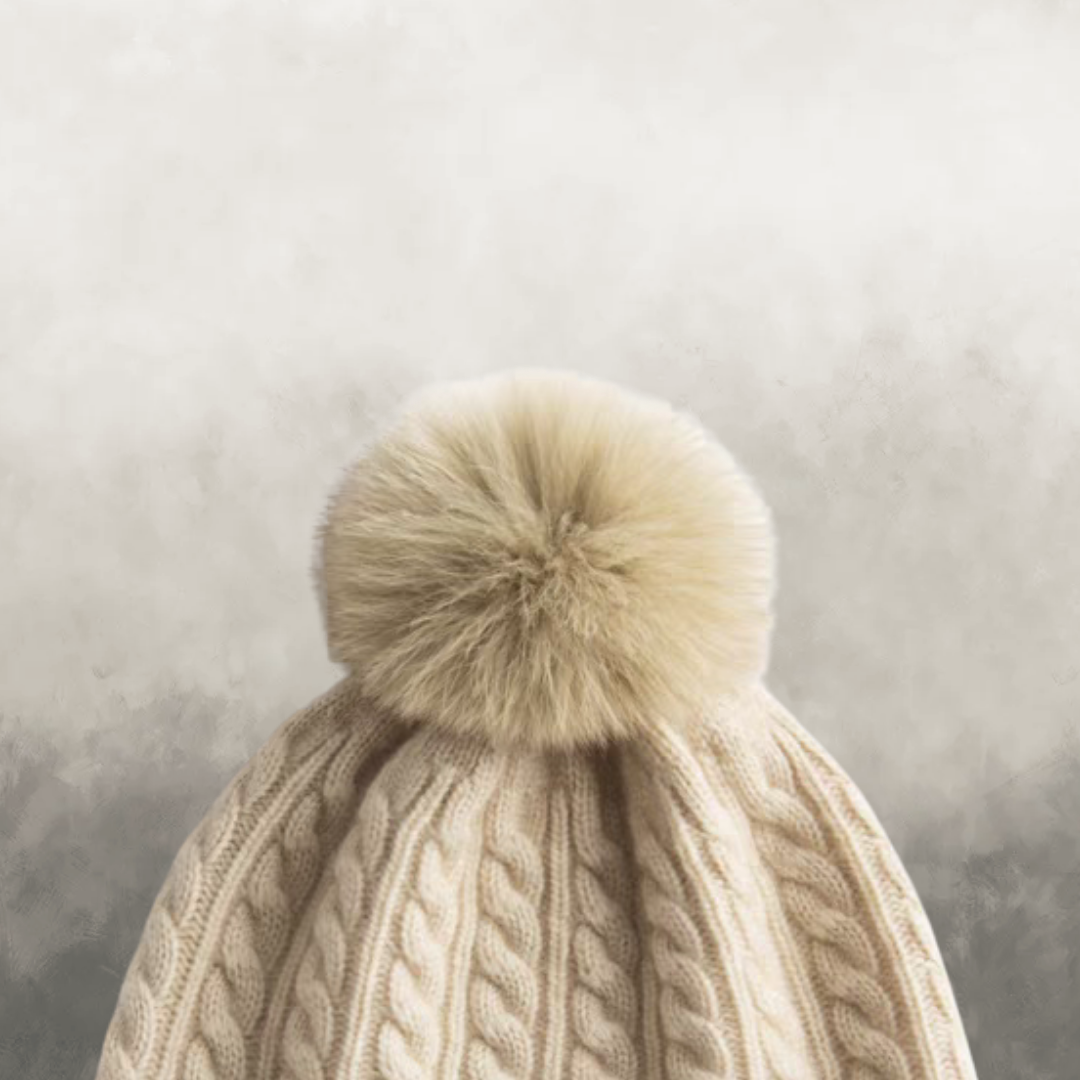 Beige knitted hat with a fluffy pom-pom against a neutral background