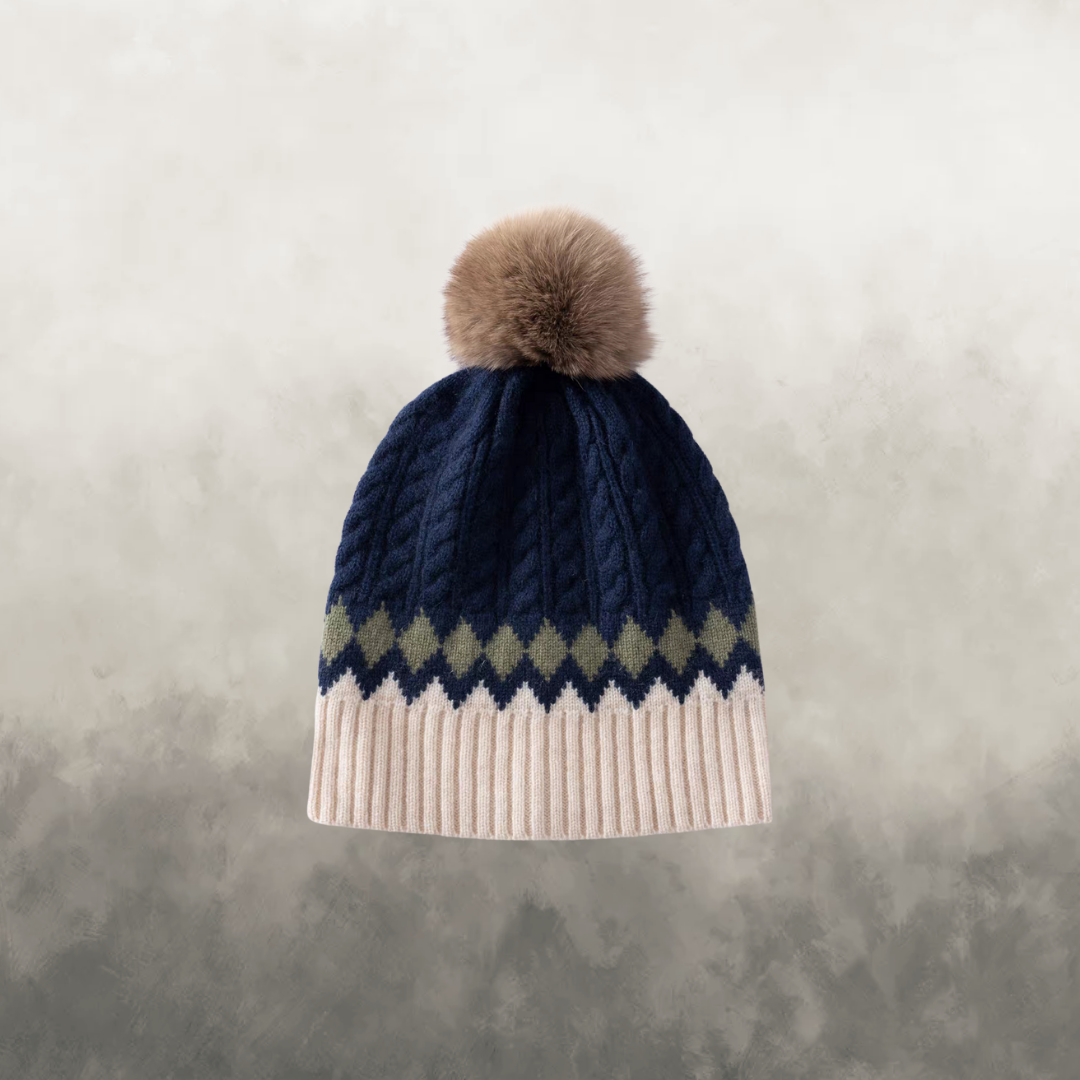 Navy blue knit beanie with a pom-pom on a textured gray background