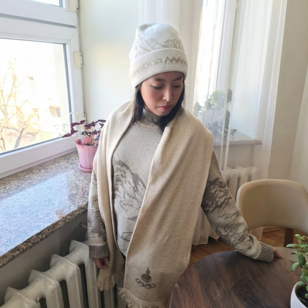 Person wearing a beige scarf and white knit hat indoors by a window