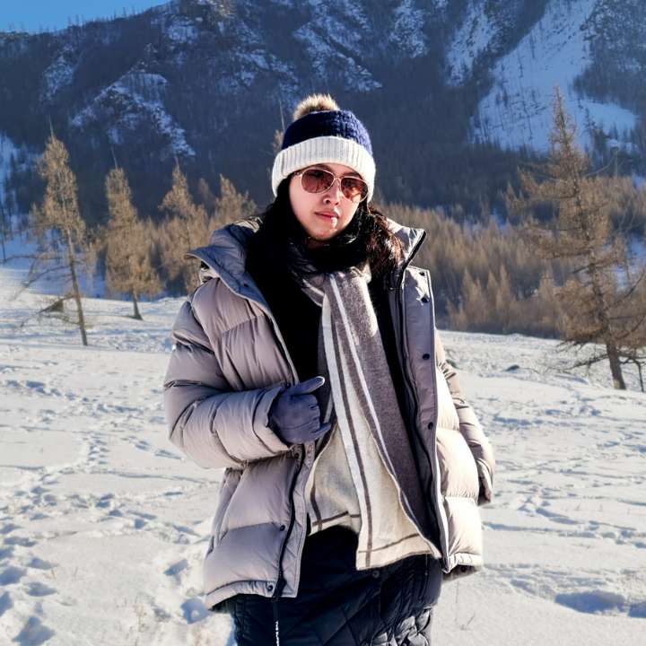 Person in winter clothing standing in a snowy landscape with mountains in the background