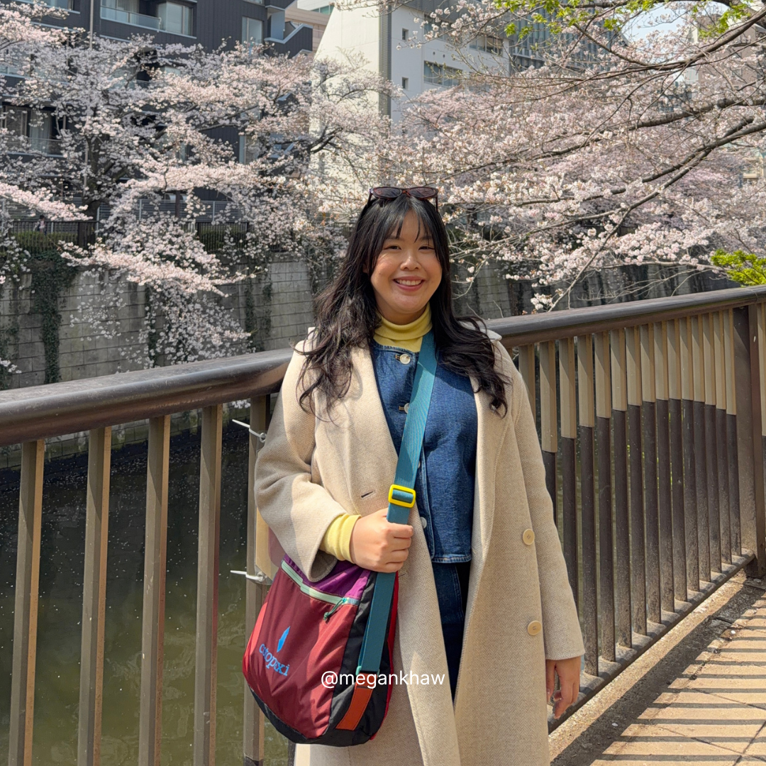 Woman standing under cherry blossom trees by a river with a herringbone wool coat