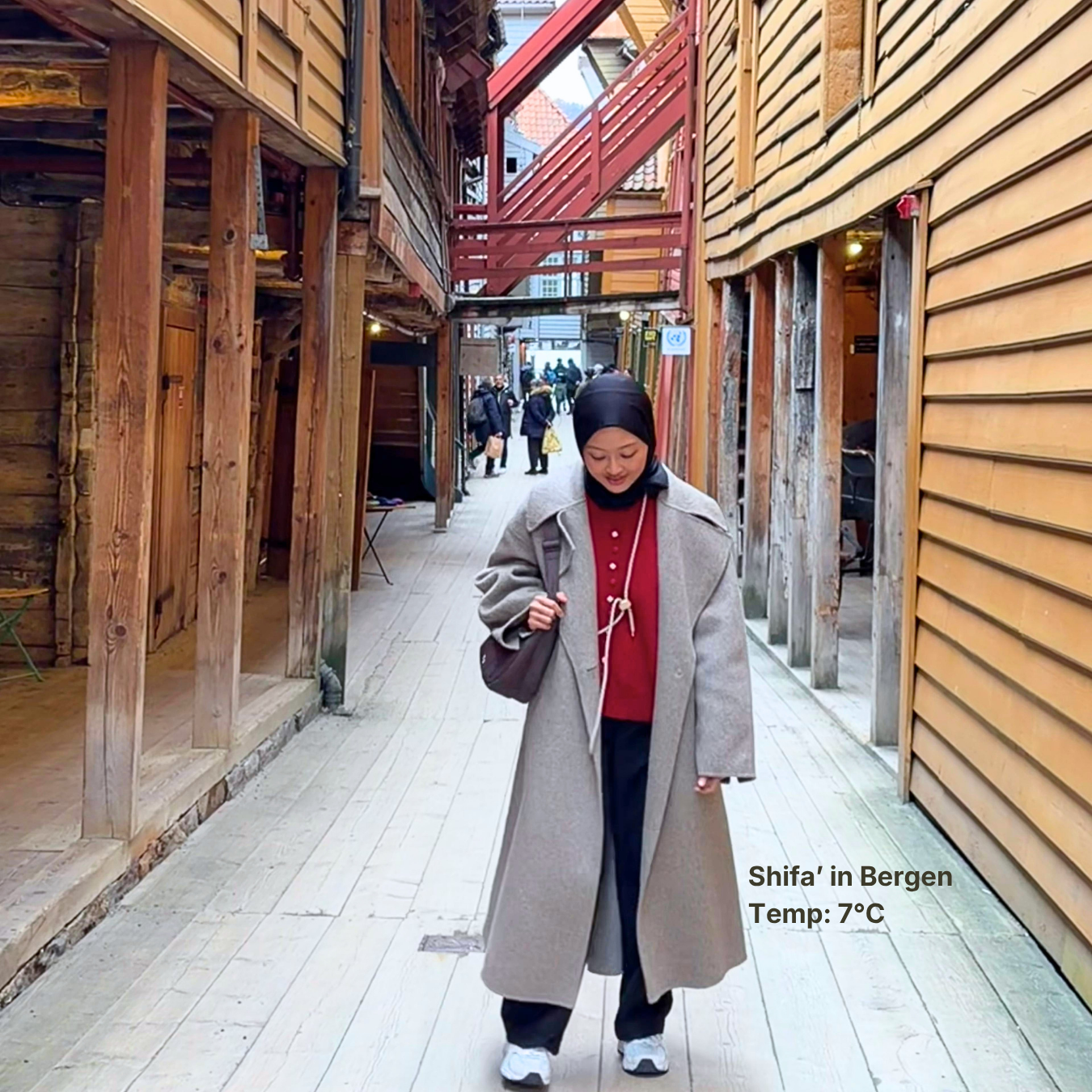 Person walking through a narrow alleyway with wooden buildings in Bergen, Norway.