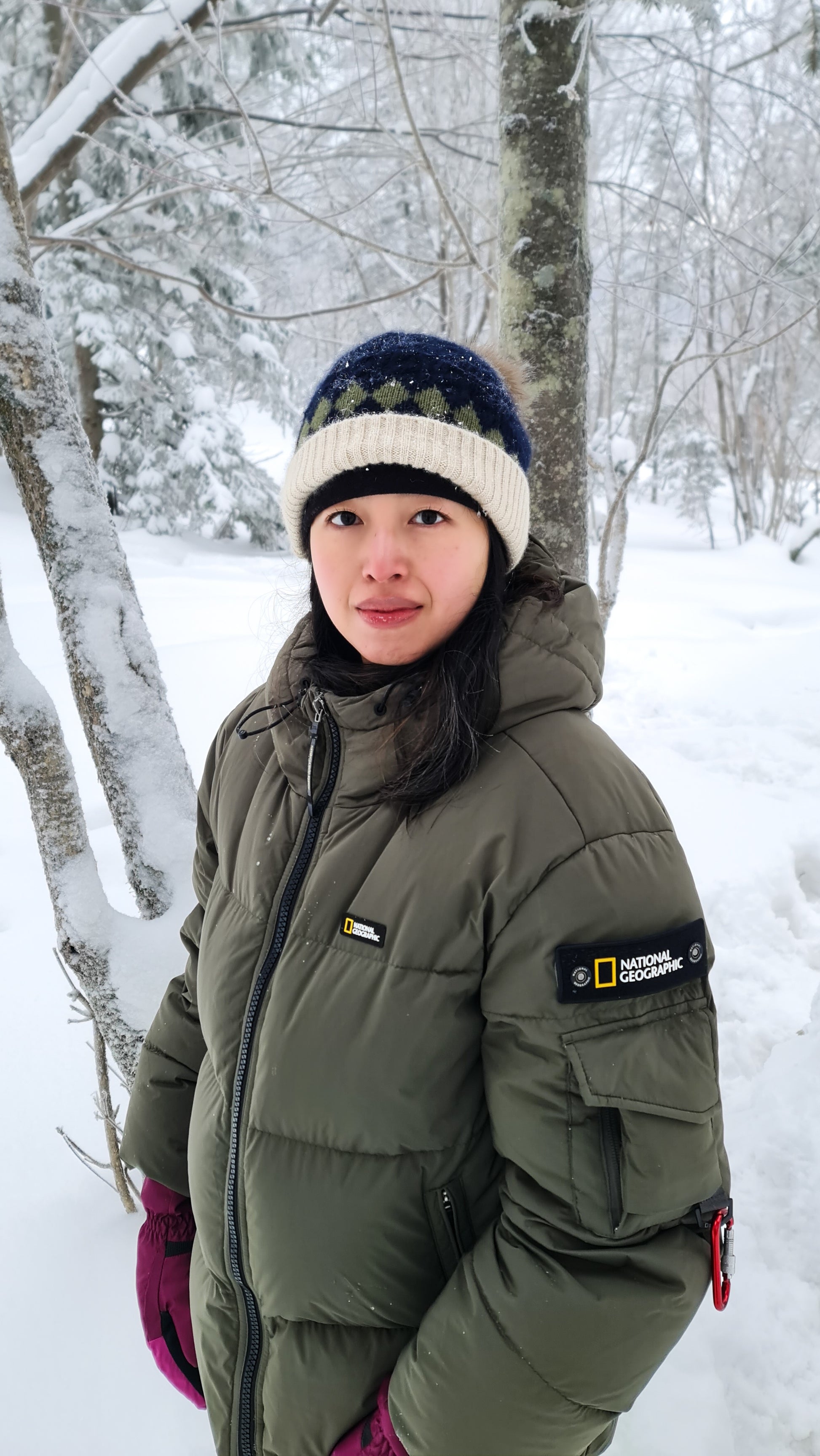 A lady wearing olive unisex puffer jacket in a snowy birch forest