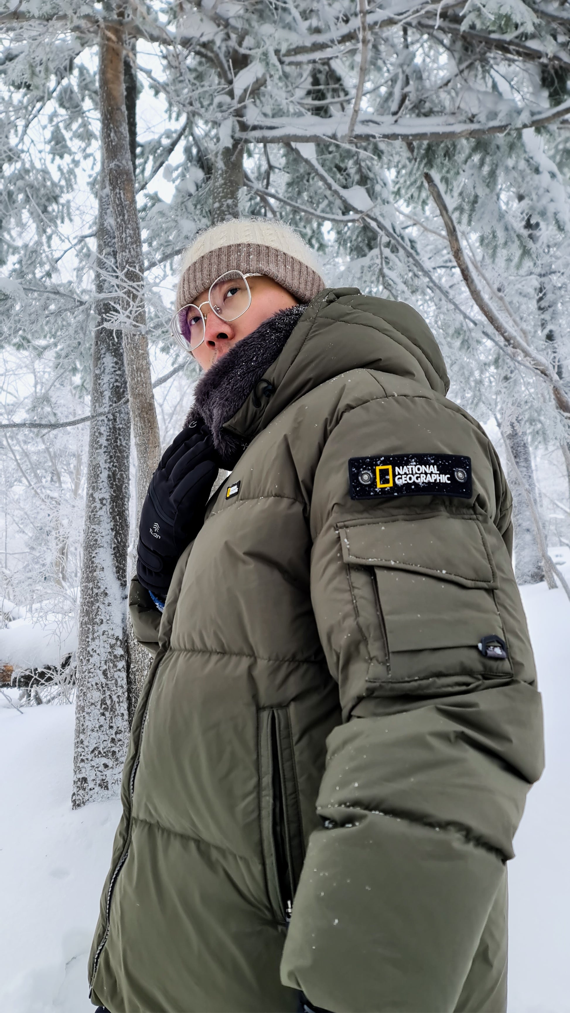 A man wearing olive unisex puffer jacket in a snowy birch forest