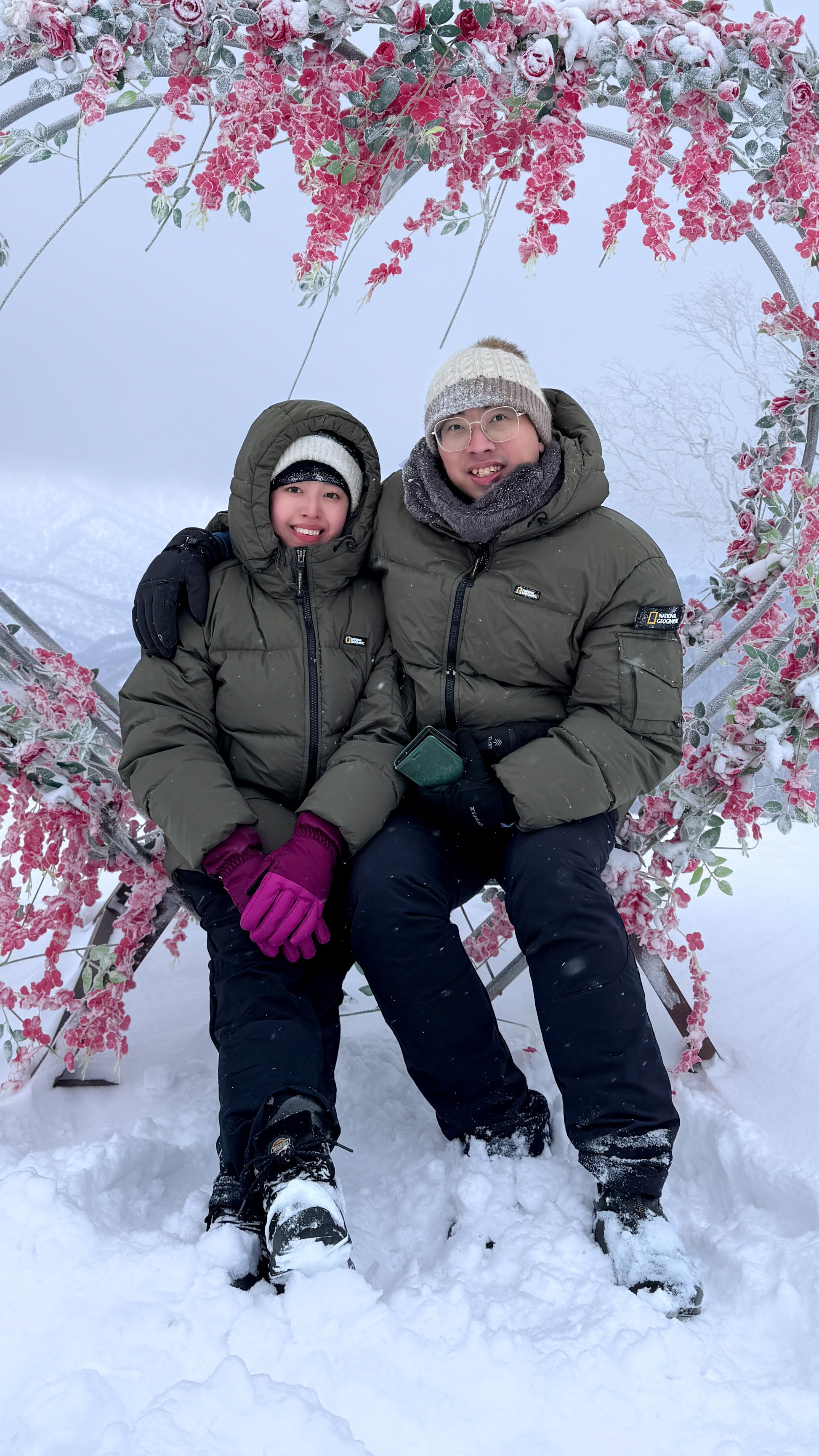 A couple wearing olive unisex puffer jacket on a heart-shaped swing