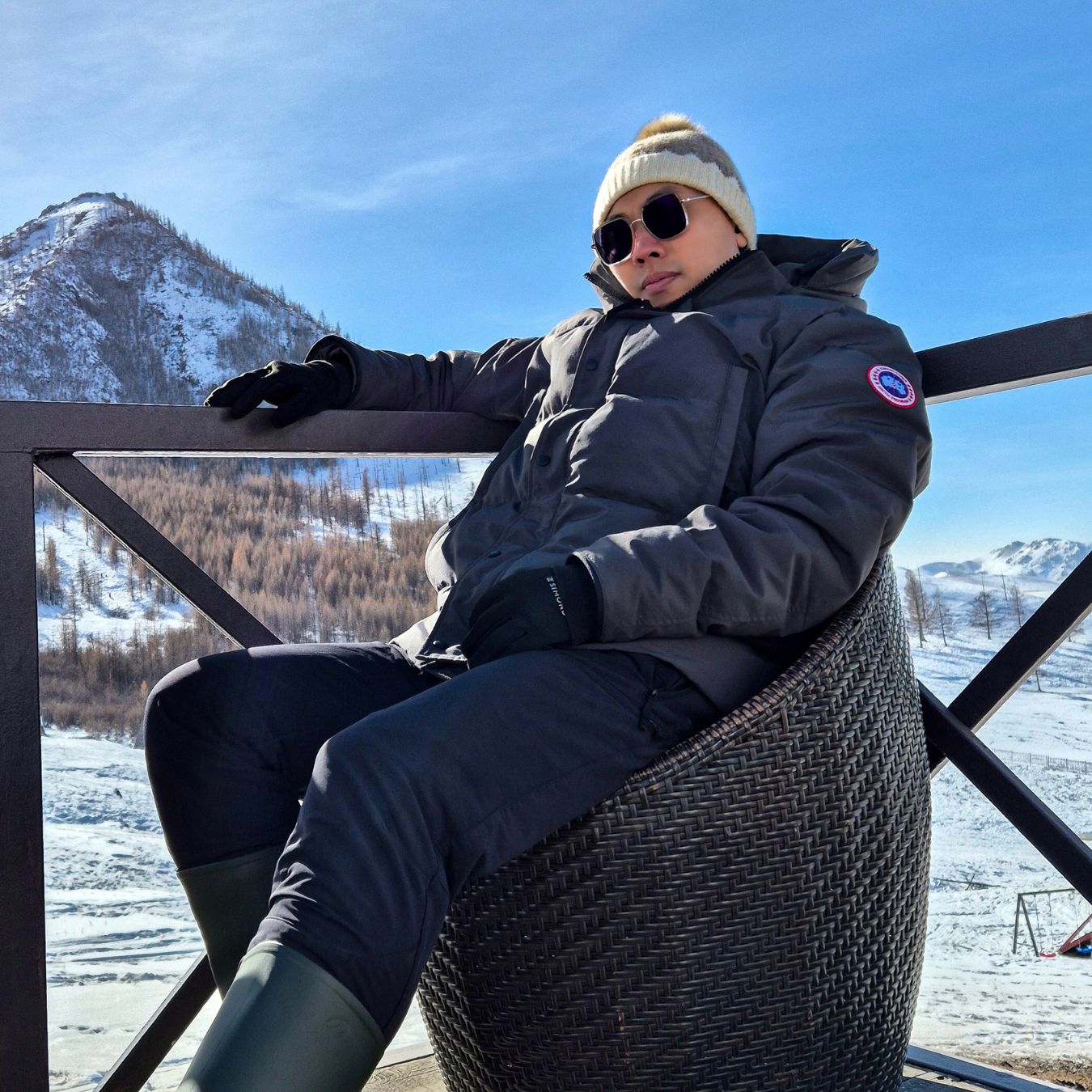 Person in winter clothing sitting on a chair with snowy mountains in the background