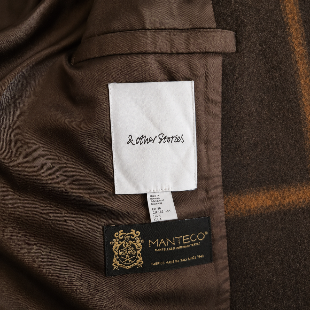 Close-up of a brown jacket interior showing a white sewn-in label reading 'Leather Stories' and a black Manteco fabric brand patch below it.