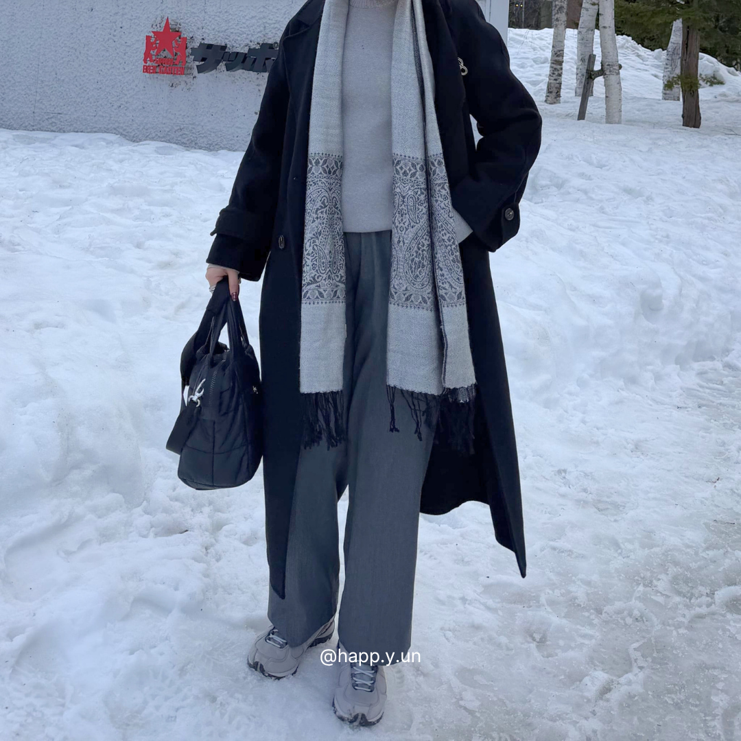 Person wearing a long coat, scarf, and holding a bag in a snowy landscape
